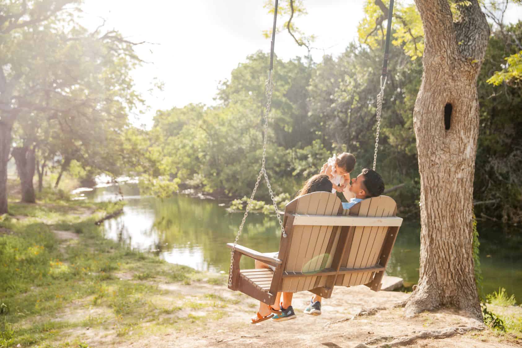 Couple on a swing overlooking a peaceful river in a park setting.