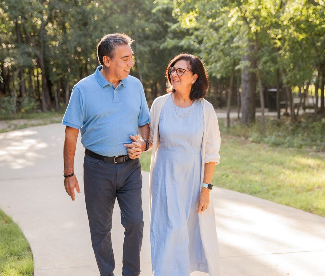 Smiling couple walking outdoors in a park on a sunny day.