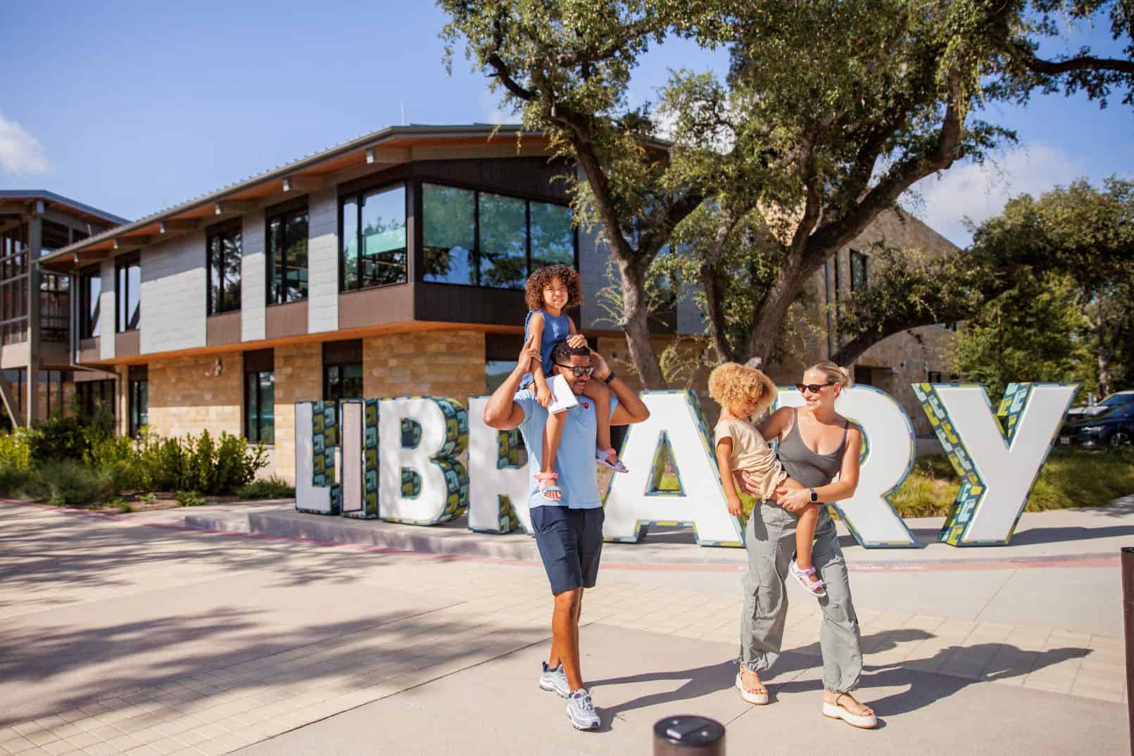 Family enjoying time outside The Bell District library with large 'LIBRARY' letters.