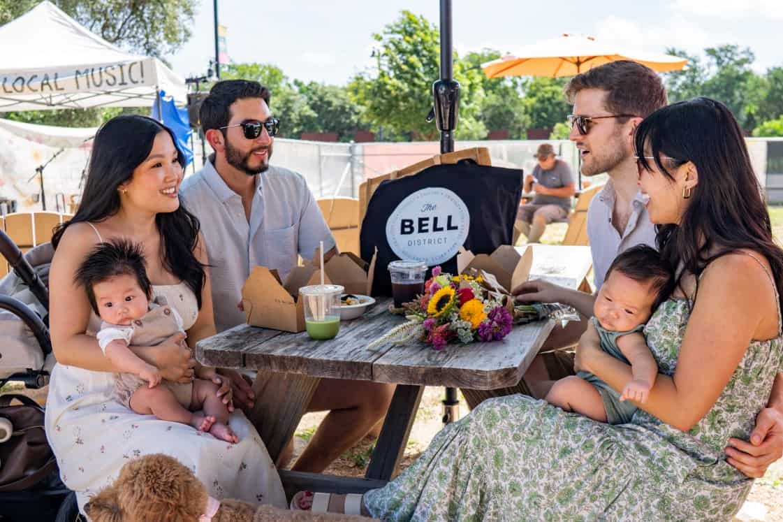 Family enjoying outdoor dining at The Bell District with live music and vibrant atmosphere.